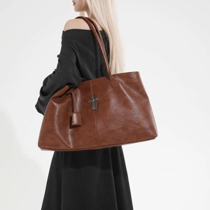 Dettaglio della borsa tote in pelle marrone scuro con ciondolo a croce vintage e capiente