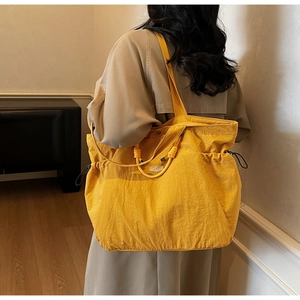 Detailed back view of a yellow nylon tote bag with side drawstrings and logo patch
