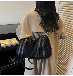 Détail du sac Boston en daim noir avec poignées en cuir et finitions dorées sur un mannequin