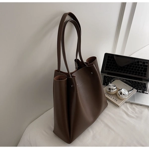 Close-up of dark brown leather tote bag showing metallic studs and workplace aesthetic