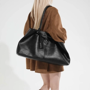 Dettaglio della borsa tote in pelle nera con ciondolo a croce argento e trama naturale