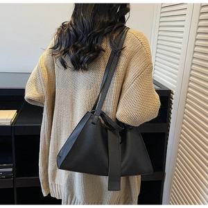Close-up of the black trapezoid shoulder bag design on a model wearing beige cardigan