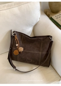 Detail of dark brown tote bag with white contrast stitching and soft pom-pom charm