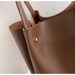 Detail shot of brown lychee-textured leather tote with silver rivets and neat stitching