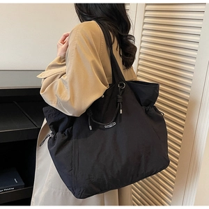 Detailed view of large black nylon tote bag featuring drawstring sides and square brand label