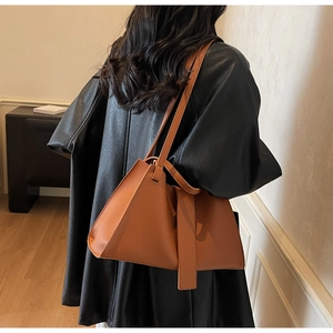 Brown lychee leather tote bag worn by model, showing side view and modern trapezoid shape
