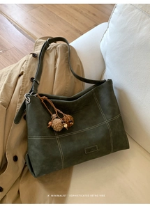Detail view of dark green matte tote bag with contrast stitching and plush ball charm