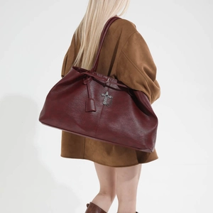 Dettaglio della borsa tote rosso scuro con ciondoli a croce e finitura in pelle martellata