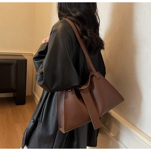Detail view of brown lychee grain leather dumpling bag on black coat worn by model