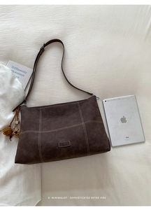 Detail of dark brown suede tote bag with contrast white stitching and tassel charm