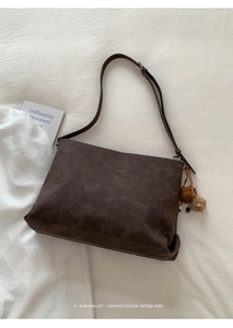 Detail of dark brown tote bag with vintage tassel charm on minimalist bedding