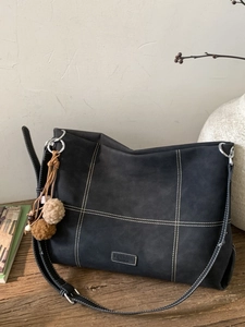 Minimalist black tote bag with white contrast stitching and plush ball charm on wooden background