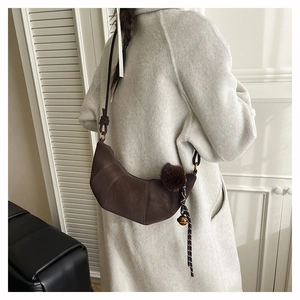Détail du sac croissant marron mat avec pompon en peluche et clochette sur manteau