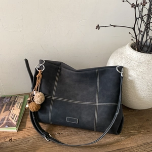 Detalle del bolso tote de ante gris con costuras en contraste y colgante de pompones