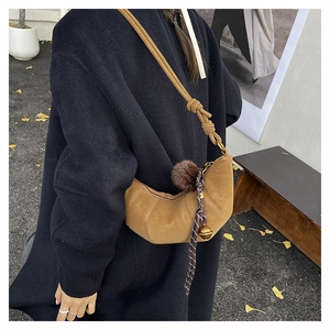 Détail du sac croissant en daim camel avec pompon et bandoulière nouée au décor d'automne