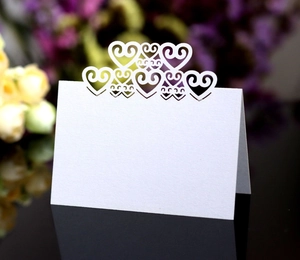 Macro detail of laser-cut hollow heart table place cards on a black reflective surface