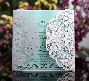 Macro view of white laser-cut lace wedding invitation with a mint green inner card insert