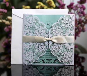 Detailed laser-cut floral invitation with mint green insert, cream ribbon, and white envelope