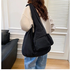 Detail of a large black utility nylon shoulder bag showing a spacious front flap pocket