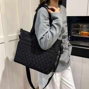Vue latérale du grand sac cabas noir matelassé porté à l'épaule avec bandoulière