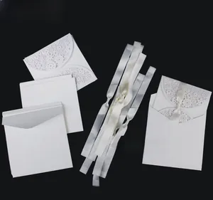 Detailed view of laser cut floral wedding invitation with white ribbon and envelope