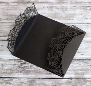 Detailed laser-cut spider web pattern on a black Halloween invitation card cover