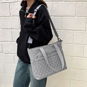 Gros plan du sac cabas matelassé gris clair avec une bandoulière bleue tissée