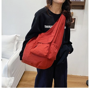 Detailed view of red nylon tote bag featuring large front flap pocket and drawstring side