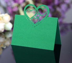 Close-up of green wedding place card with laser-cut hollow heart design on black mirror