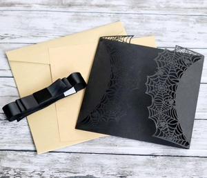 Detail of laser-cut black spider web invitation with kraft envelope and silk ribbon