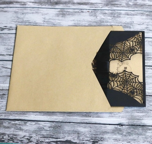 Detail view of laser-cut black spider web invitation card with kraft paper envelope