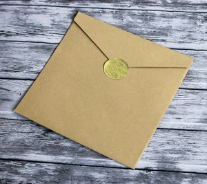 Close-up of kraft paper envelope with gold embossed seal sticker and invitation text