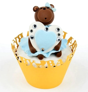 Detail of yellow laser-cut cupcake wrapper with BABY text and a blue ribbon teddy bear