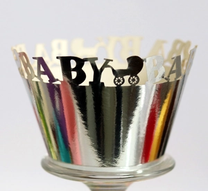 Macro view of silver laser-cut cupcake wrappers with BABY text and stroller motifs