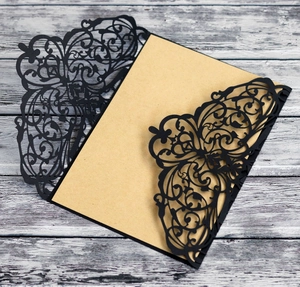 Laser cut black invitation card with elegant vine patterns on vintage wood background