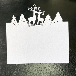 Detailed laser-cut Christmas reindeer and forest silhouettes on a white paper place card