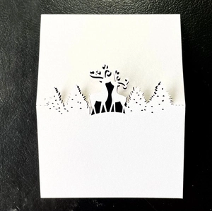 Close-up of laser-cut white Christmas place card featuring reindeer and forest silhouette