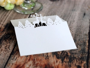 Laser-cut white reindeer Christmas table card with forest silhouette on vintage wood