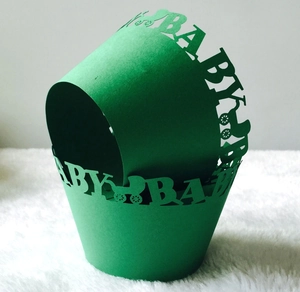 Detail of green laser-cut cupcake wrappers with hollow baby carriage and BABY text design