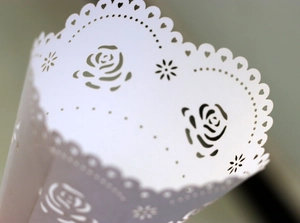 Close-up of laser-cut white paper cones with rose patterns and heart lace for weddings