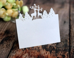 Detail of laser-cut white pearlescent paper place card with reindeer and pine tree design