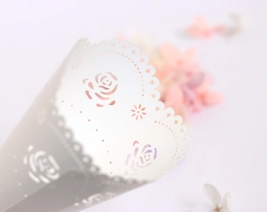 Detailed close-up of white laser-cut wedding paper cone with rose and heart patterns