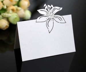 Macro detail of white pearlescent table card with laser-cut lily flower design for weddings