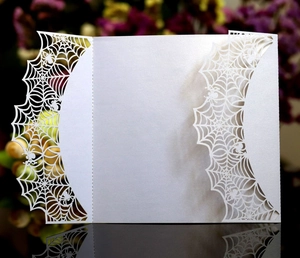 Detail of laser-cut white spider web invitation card with precise gothic spider patterns