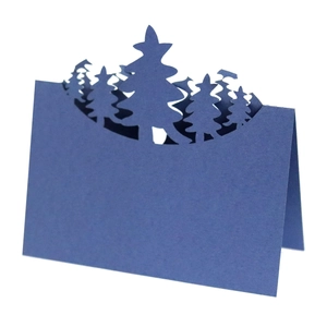 Detail of laser-cut dark blue place card with 3D forest pine tree design on white background