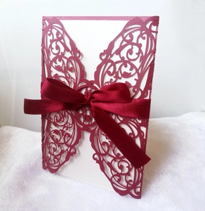 Intricate laser-cut butterfly wedding invitation in deep red with a matching satin ribbon