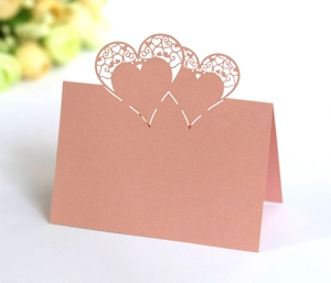 Detail of rose gold laser-cut heart place card with intricate vine hollow pattern on desk