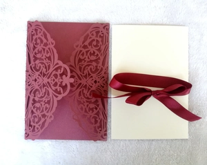 Close-up of laser-cut burgundy wedding invitation with intricate vine patterns and ribbon