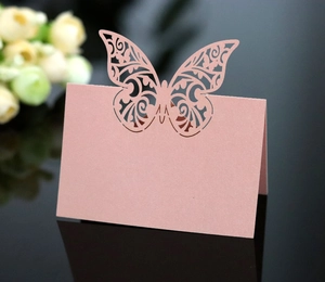 Detail of pink laser-cut butterfly place card on reflective surface with flowers
