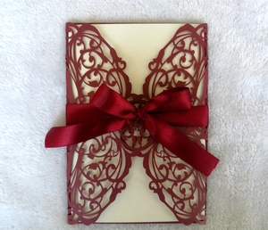 Macro view of burgundy laser-cut butterfly invitation with silk ribbon on soft plush fabric